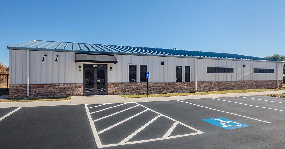 Single-story metal office building with stone base, glass entry doors, and accessible parking in front.